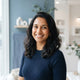 A professional portrait of a smiling South Asian woman, reflecting a satisfied customer in a modern, light-filled setting.
